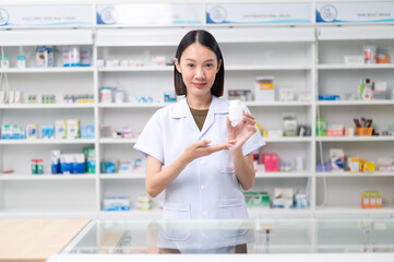 Wall Mural - Asian professional female pharmacist standing with arms crossed looking at camera charming smile pointing hand to pill bottle health care products in pharmacies Close-up and wide-angle shots