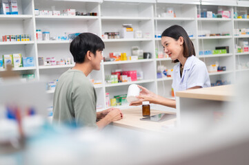 Wall Mural - Asian professional female pharmacist using a digital tablet computer to dispense prescription medication to male customers. The doctor advises and explains to the client about the medication.