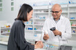 © PhugunStock - Asian professional male pharmacist using a tablet to dispense prescription medicines to female customers. The doctor advises and explains to the client how to use the medication.