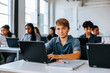 © Maskot - Portrait of teenage boy sitting with laptop near desk in classroom at school