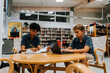 © Maskot - Focused male students studying while sitting near table in library at junior high school