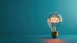© solidmaks - Illuminated light bulb with ‘2025’ filament on dark blue back