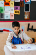 © Maskot - Focused boy painting on paper while sitting near desk at art class in school
