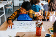 © Maskot - Focused boy doing finger painting on paper during art class at elementary school