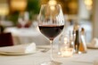 © inspiretta - A wine glass is filled with red wine on a table. The wine glass is on a table with a white tablecloth and a candle in the middle of the table