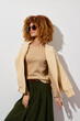 © SHOTPRIME STUDIO - Fashionable mannequin with curly hair wearing a beige top and a light cardigan against a white background Modern style, trendy outfit, showcasing contemporary fashion concepts