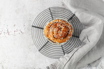 Wall Mural - Freshly baked cinnamon bun roll closeup on retro metal baking rack with grey linen napkin on grunge stone table background.