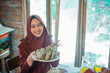 © Odua Images - attractive woman in hijab showing ketupat during Eid with a simple house background