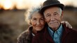 © familymedia - A senior couple embraces lovingly outdoors during a sunset, the warm glow highlighting their gentle expressions and evoking a sense of enduring affection.