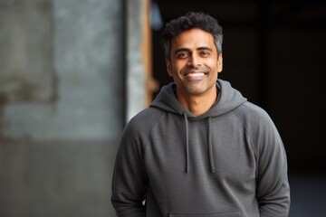 Wall Mural - Portrait of a cheerful indian man in his 30s dressed in a comfy fleece pullover isolated in empty modern loft background