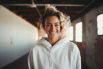 Wall Mural - Portrait of a grinning woman in her 20s wearing a zip-up fleece hoodie over empty modern loft background