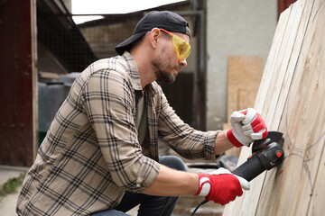 Poster - Man grinding wooden planks with angle grinder outdoors