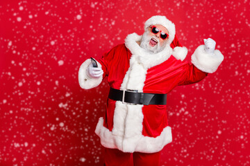 Poster - Portrait of crazy santa claus in hat using cell phone device raising fists screaming yes having newyear party wearing belt eyewear eyeglasses isolated over red background