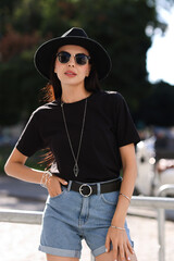 Poster - Young woman in stylish black hat and sunglasses on city street