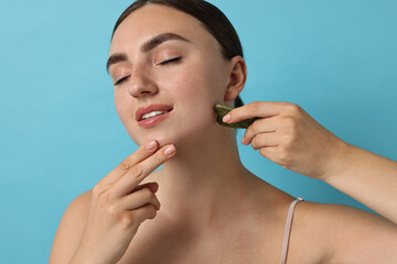 Poster - Beautiful young woman doing facial massage with gua sha tool on light blue background