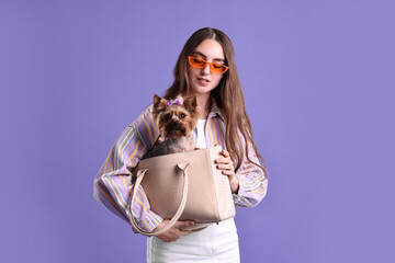 Wall Mural - Beautiful young woman carrying cute Yorkshire Terrier dog in bag on violet background