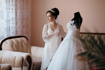 A woman is standing in front of a white dress and a mannequin. The woman is wearing a white gown and a veil. She is looking at the dress