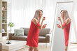 © Ljupco Smokovski - Young woman in a red dress putting on lip gloss in front of a mirror