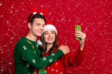 Poster - Portrait of two peaceful cheerful people embrace hold telephone make selfie isolated on red color background