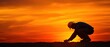© Rossarin - Construction worker examining ground at sunset, silhouette against fiery sky.