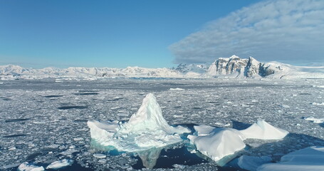 Wall Mural - Beautiful iceberg floating arctic ocean under blue sky. Wild nature winter aerial landscape panorama. Ice floe formation drifts polar sea. Snow covered mountains in background. Ecology, climate change