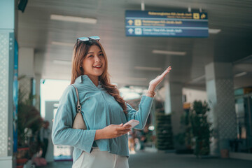 A cheerful and vibrant young woman holding her smartphone at a busy airport terminal