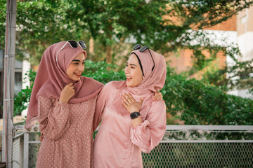 Two cheerful friends in colorful hijabs share a joyful moment in an open outdoor space