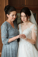 Wall Mural - A woman in a wedding dress is standing next to her mother. The mother is holding the bride's hand and looking at her. Scene is one of love and support