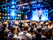 © sanjit536 - Business Conference Speaker Presenting to a Large Audience in a Professional Setting, on dark blue background