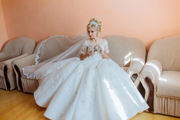 A bride is getting ready for her wedding and is looking at a dress in a mirror. The dress is white and has a lace design. The bride is wearing a white robe and a tiara