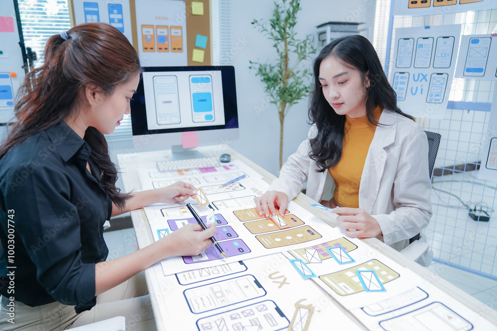 Two female ui/ux designers are working together in the office, using a ...