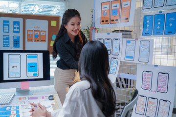 Two asian women working as ui/ux designers discussing over new mobile application interface wireframe design together in modern office