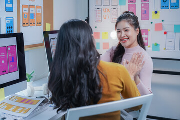 two young asian ui/ux designers are giving high five in the office, celebrating the success of their