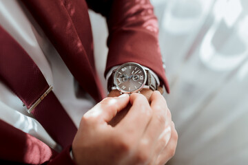 a man in a red suit is wearing a watch and adjusting it. the watch is silver and has a black face. t