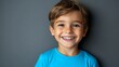 © Maria Mikhaylichenko - Joyful young boy with bright smile and sparkling eyes wearing vibrant blue t-shirt against dark background, radiating happiness and innocence in portrait.