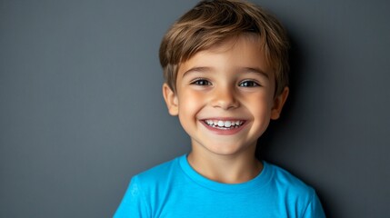 joyful young boy with bright smile and sparkling eyes wearing vibrant blue t-shirt against dark back