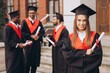 © anatoliycherkas - Joyful Young Woman Celebrating Graduation with Friends in Academic Gowns Outdoors