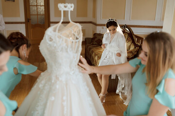 A bride is getting ready for her wedding and her bridesmaids are helping her. One of the bridesmaids is holding a dress up to the bride's face