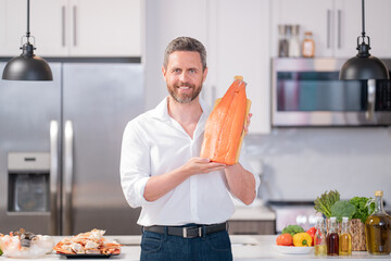 Poster - Millennial hispanic man hold salmon fillet at kitchen. Cooking salmon fillet. Restaurant menu with salmon fillet. Cooking, advertising salmon fillet concept.