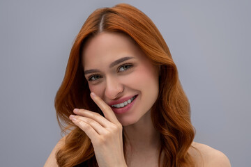 Cute young woman with long ginger hair on a grey background