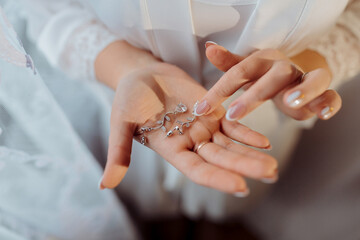 A woman is holding a pair of earrings in her hand. The earrings are silver and have a design that resembles a flower. The woman is wearing a white dress and a veil