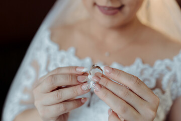 A woman is holding a ring in her hand. The ring is gold and has a diamond on it. She is wearing a white wedding dress