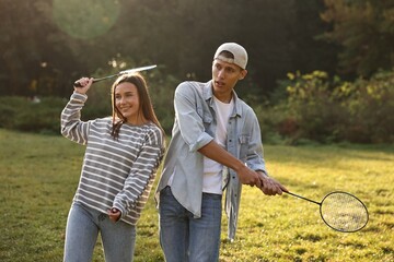 Wall Mural - Young woman and man playing badminton in park on sunny day