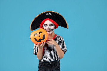 Wall Mural - Funny boy with pumpkin bucket dressed like pirate on light blue background. Halloween costume