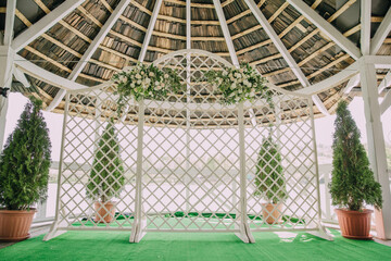 A beautiful white archway with a white lattice is set up in a garden. The archway is surrounded by two white potted plants, one on each side. The archway is decorated with white flowers