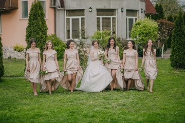 A group of women are walking in a field, one of them is wearing a white dress. The bride is holding a bouquet of flowers