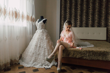 A woman in a pink gown sits on a bed next to a white dress. The room is decorated with a zebra print wall covering