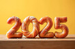© Irina - Buns with sugar in the shape of the numbers 2025 on a wooden table, yellow background. A signboard template for a bakery for the New Year holidays.