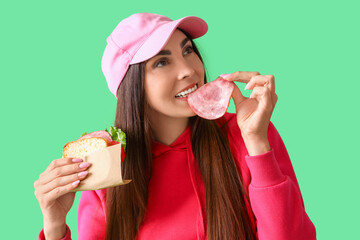 Wall Mural - Young woman eating tasty sandwich on green background, closeup