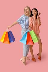 Poster - Beautiful young women with shopping bags on pink background